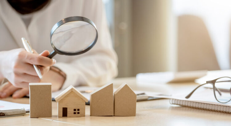 Looking for real estate agency, property insurance, mortgage loan or new house. Woman with magnifying glass over a wooden house at her office